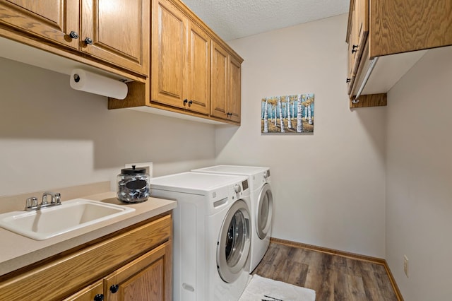 clothes washing area with a textured ceiling, a sink, independent washer and dryer, cabinet space, and dark wood finished floors