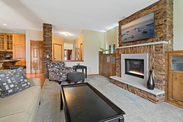 living area with baseboards, light colored carpet, a textured ceiling, and a glass covered fireplace