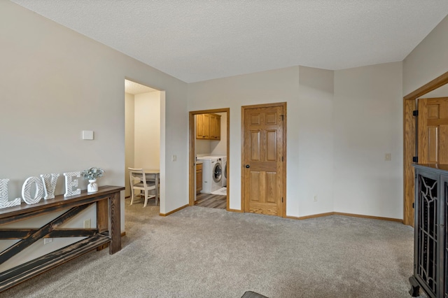 interior space with baseboards, washer / clothes dryer, a textured ceiling, and light colored carpet