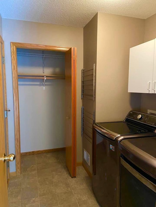 clothes washing area with washer and clothes dryer, cabinets, and a textured ceiling