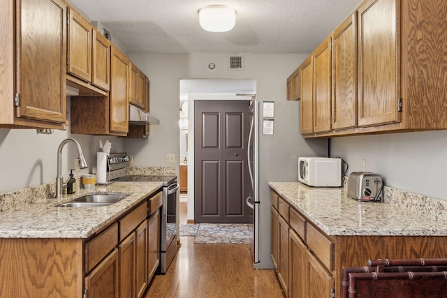 kitchen featuring sink, light stone counters, stainless steel appliances, a textured ceiling, and light hardwood / wood-style flooring