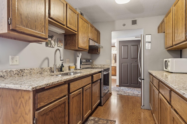 kitchen featuring sink, a textured ceiling, light wood-type flooring, stainless steel electric stove, and light stone countertops