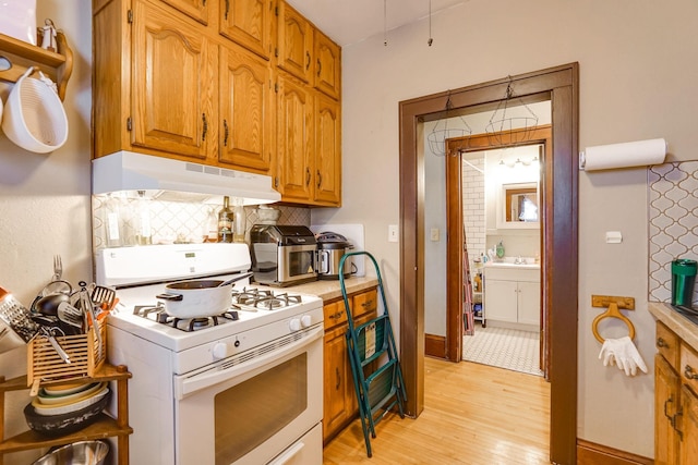 kitchen featuring white gas range, light hardwood / wood-style floors, and backsplash