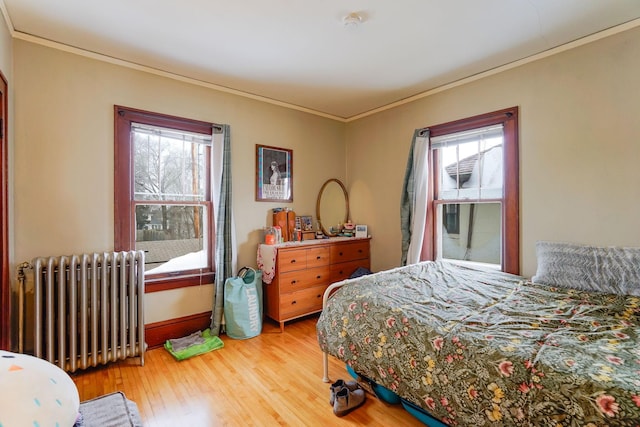 bedroom featuring hardwood / wood-style floors, ornamental molding, radiator heating unit, and multiple windows