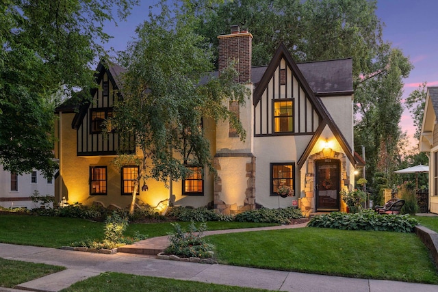 tudor-style house featuring a lawn, a chimney, and stucco siding