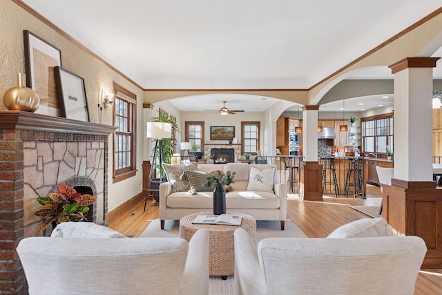 living area featuring ornate columns, light wood finished floors, a fireplace, arched walkways, and ceiling fan