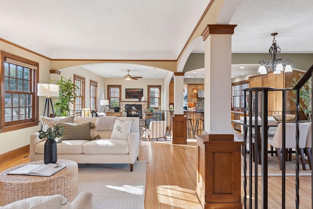 living room with light wood-style flooring, arched walkways, a fireplace, baseboards, and ceiling fan