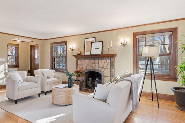 living area with wood finished floors, arched walkways, a stone fireplace, baseboards, and a textured wall