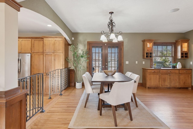 dining area featuring light wood-type flooring, arched walkways, a chandelier, and french doors