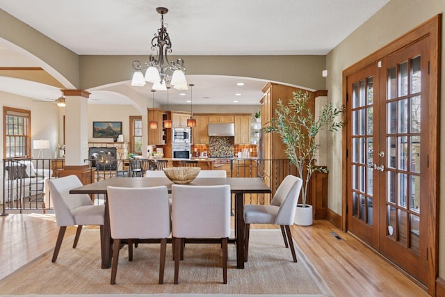 dining area featuring recessed lighting, french doors, arched walkways, a stone fireplace, and light wood finished floors