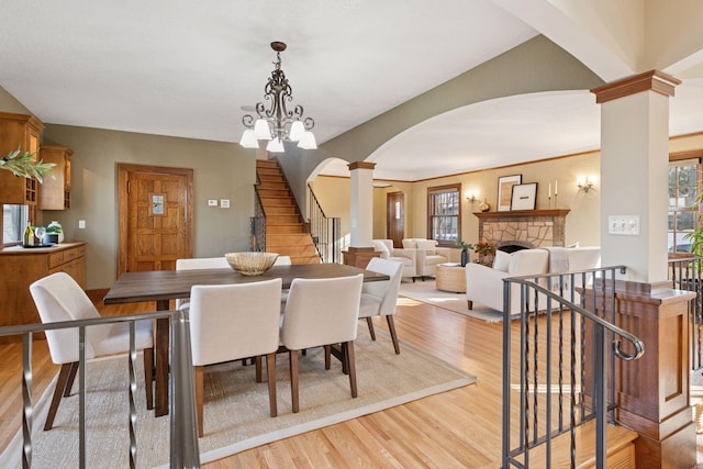 dining space with stairway, light wood-type flooring, a fireplace, arched walkways, and ornate columns