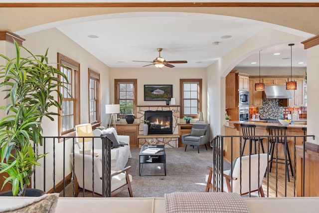 living room with a fireplace, a ceiling fan, arched walkways, and light colored carpet