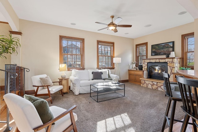 carpeted living room with a stone fireplace, a ceiling fan, and baseboards