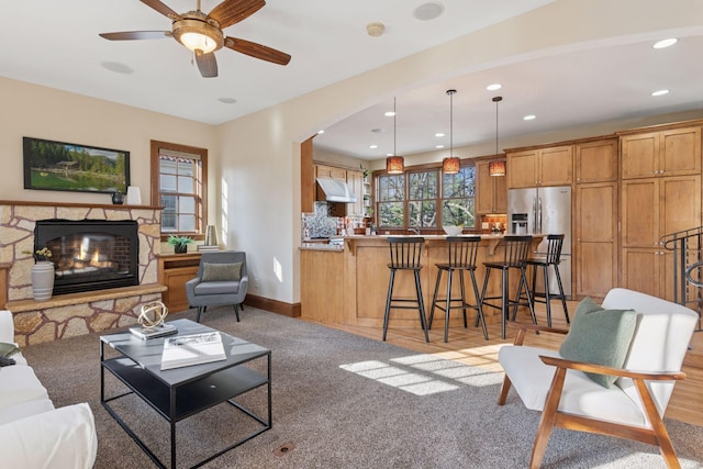 living area with baseboards, a fireplace, arched walkways, ceiling fan, and light carpet