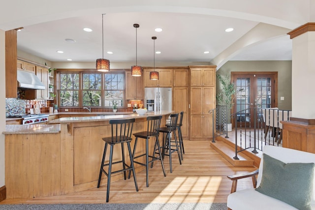 kitchen with stove, under cabinet range hood, light wood-type flooring, stainless steel refrigerator with ice dispenser, and arched walkways