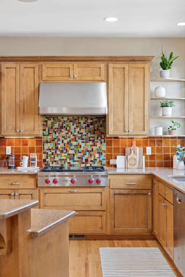 kitchen featuring light stone counters, open shelves, light wood-style floors, appliances with stainless steel finishes, and wall chimney range hood