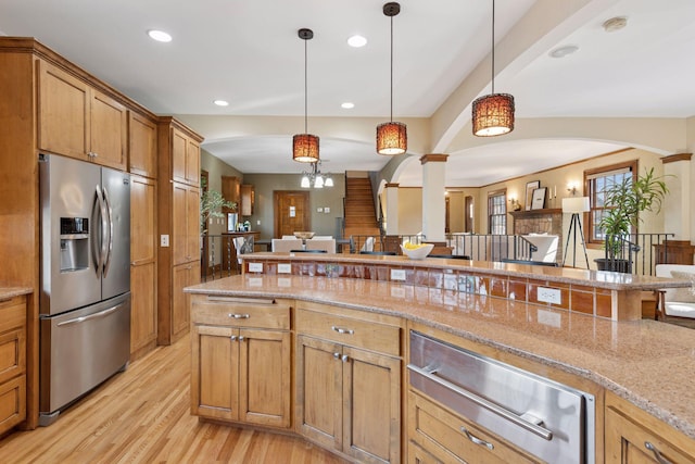 kitchen featuring open floor plan, light stone counters, light wood-style floors, stainless steel refrigerator with ice dispenser, and hanging light fixtures