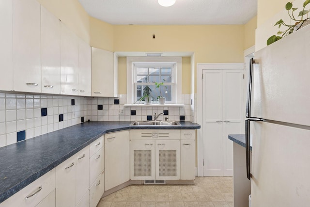 kitchen with dark countertops, backsplash, freestanding refrigerator, and a sink