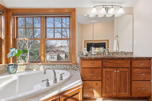 bathroom with decorative backsplash, a tile fireplace, vanity, and a garden tub