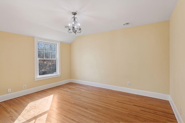 spare room with a chandelier, light wood finished floors, baseboards, and lofted ceiling