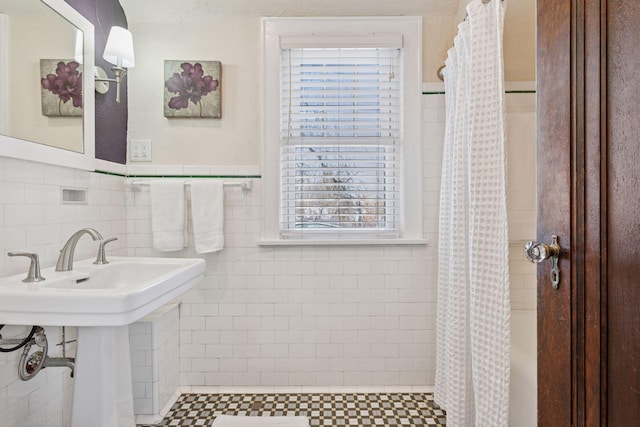 bathroom with a sink, tile walls, wainscoting, and a tile shower