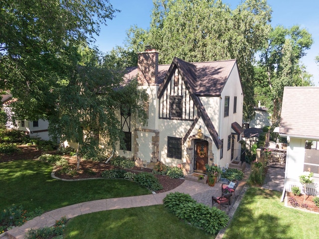 tudor home with a front lawn, a chimney, stone siding, and stucco siding