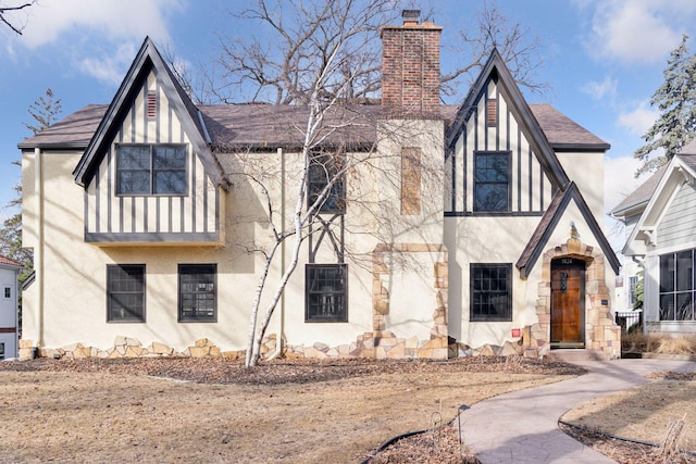 english style home with a shingled roof, a chimney, and stucco siding