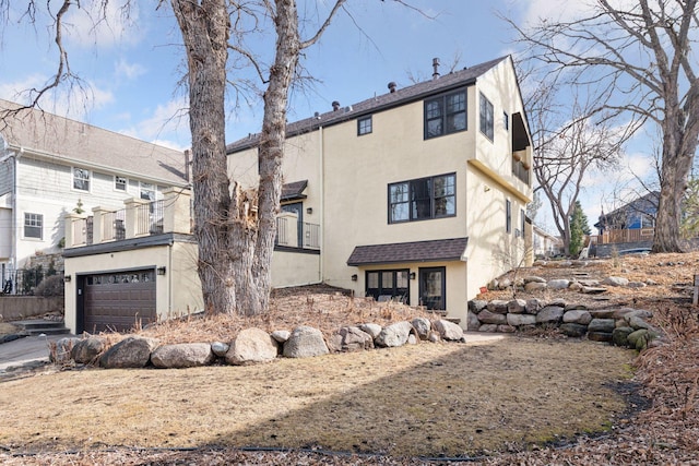 rear view of house featuring stucco siding, driveway, roof with shingles, and an attached garage