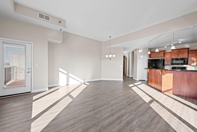 kitchen with an inviting chandelier, hanging light fixtures, a kitchen breakfast bar, black appliances, and dark hardwood / wood-style flooring