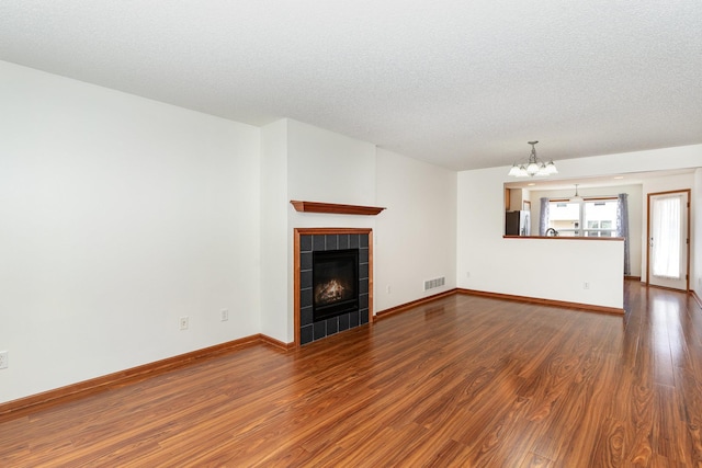 unfurnished living room with baseboards, a tile fireplace, dark wood-type flooring, a textured ceiling, and a notable chandelier