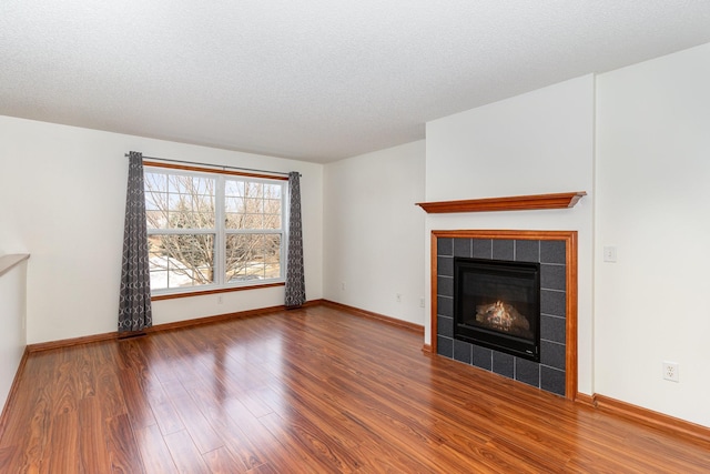 unfurnished living room featuring a tile fireplace, a textured ceiling, baseboards, and wood finished floors