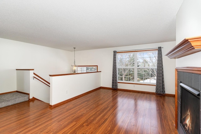 unfurnished living room with a textured ceiling, a fireplace, wood finished floors, and baseboards