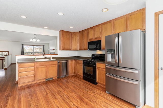 kitchen featuring dark countertops, brown cabinetry, a sink, wood finished floors, and black appliances