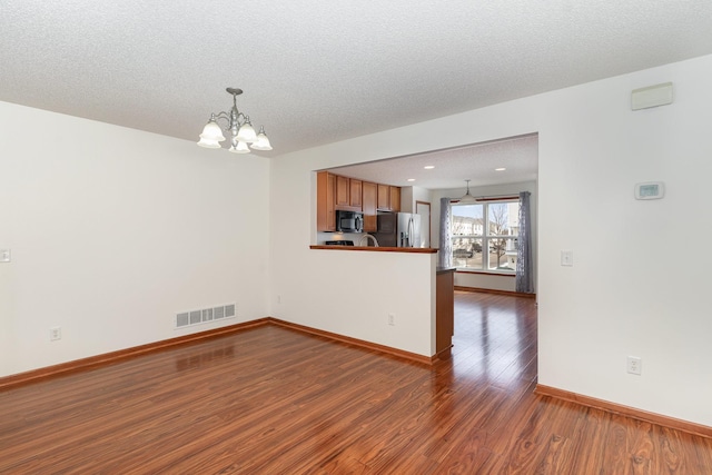 unfurnished room featuring a textured ceiling, wood finished floors, visible vents, baseboards, and an inviting chandelier