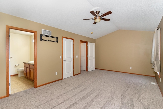 unfurnished bedroom with lofted ceiling, light colored carpet, visible vents, connected bathroom, and a textured ceiling