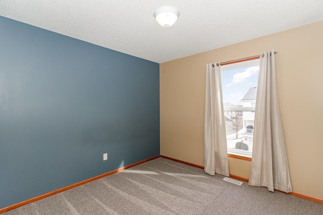 carpeted empty room featuring visible vents, a textured ceiling, and baseboards