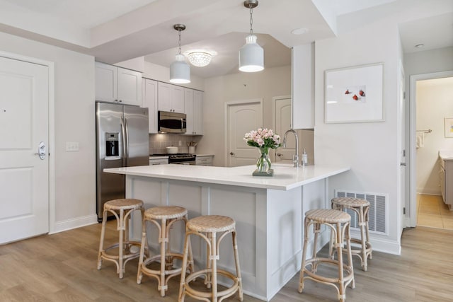 kitchen featuring pendant lighting, a kitchen breakfast bar, stainless steel appliances, tasteful backsplash, and kitchen peninsula