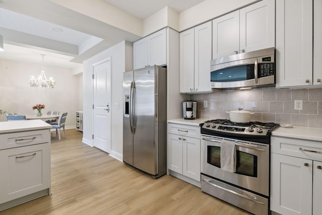 kitchen with appliances with stainless steel finishes, white cabinets, decorative backsplash, hanging light fixtures, and light wood-type flooring