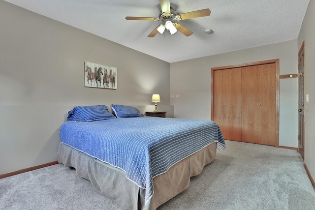 bedroom with a textured ceiling, light colored carpet, a closet, and ceiling fan