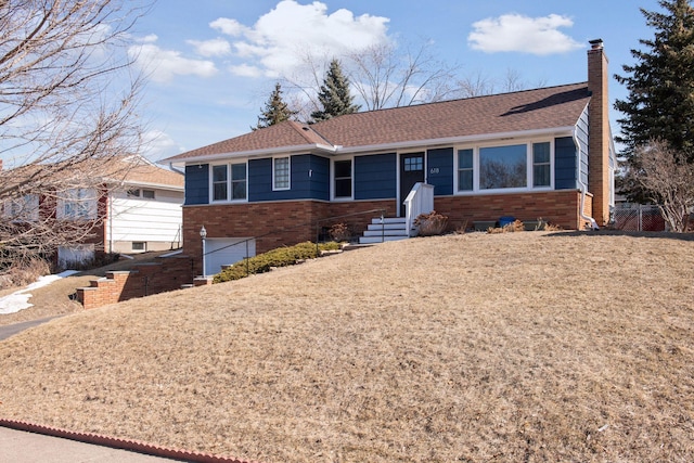 ranch-style house with a shingled roof, brick siding, and a chimney