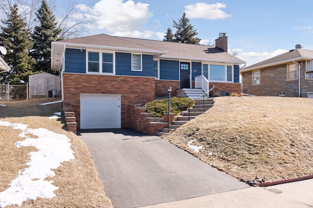 view of front of home featuring brick siding, an attached garage, fence, a chimney, and driveway