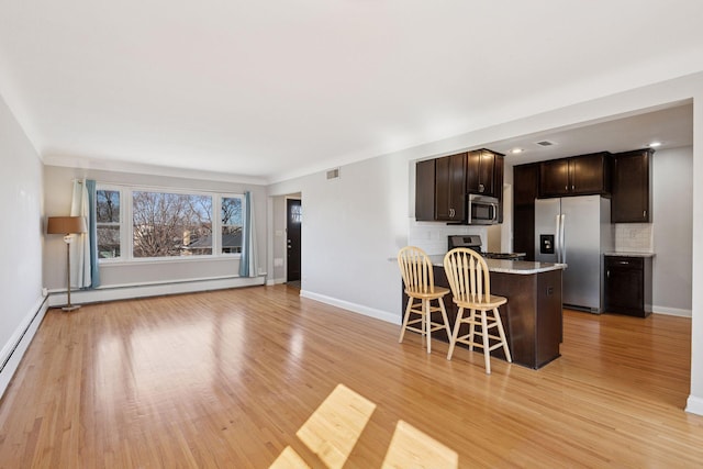 kitchen with backsplash, dark brown cabinetry, a breakfast bar, appliances with stainless steel finishes, and light wood-style floors