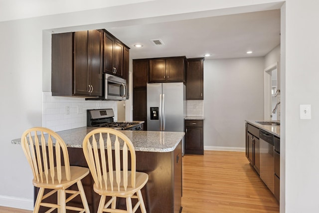 kitchen featuring visible vents, dark brown cabinets, light wood-type flooring, appliances with stainless steel finishes, and a peninsula