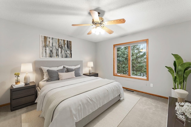 bedroom with ceiling fan, light colored carpet, and a textured ceiling