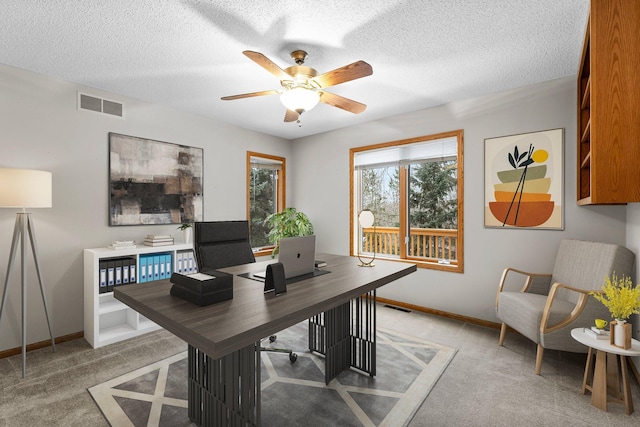 carpeted home office with ceiling fan and a textured ceiling