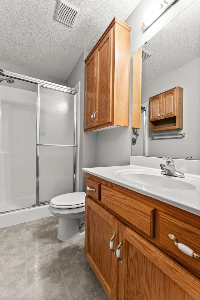 bathroom featuring vanity, toilet, a textured ceiling, and a shower with shower door