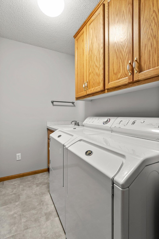 clothes washing area with washer and clothes dryer, cabinets, and a textured ceiling