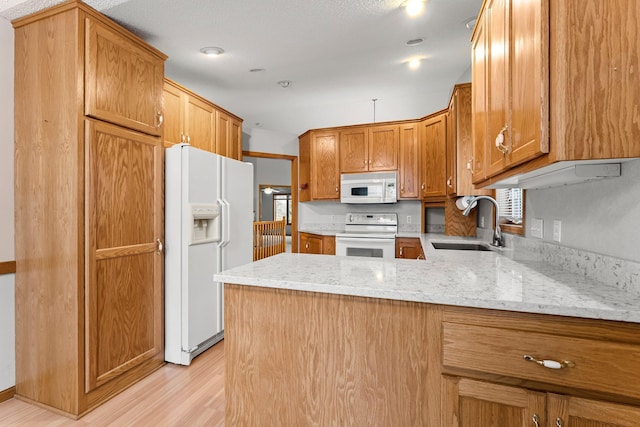 kitchen featuring sink, white appliances, light stone counters, kitchen peninsula, and light wood-type flooring