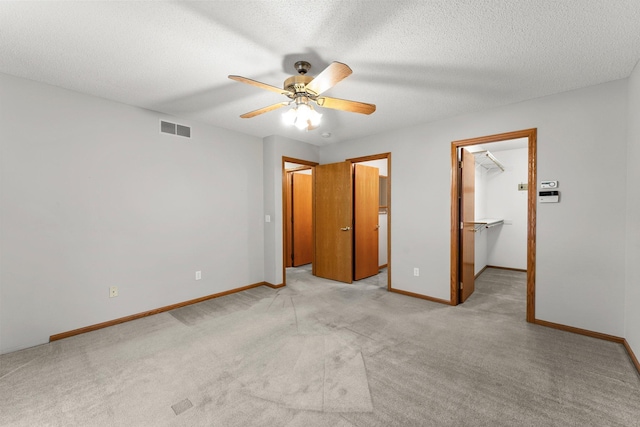 unfurnished bedroom with ceiling fan, a textured ceiling, a spacious closet, light colored carpet, and a closet