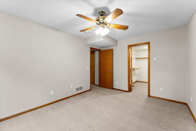 unfurnished bedroom with ceiling fan, a textured ceiling, a spacious closet, light colored carpet, and a closet